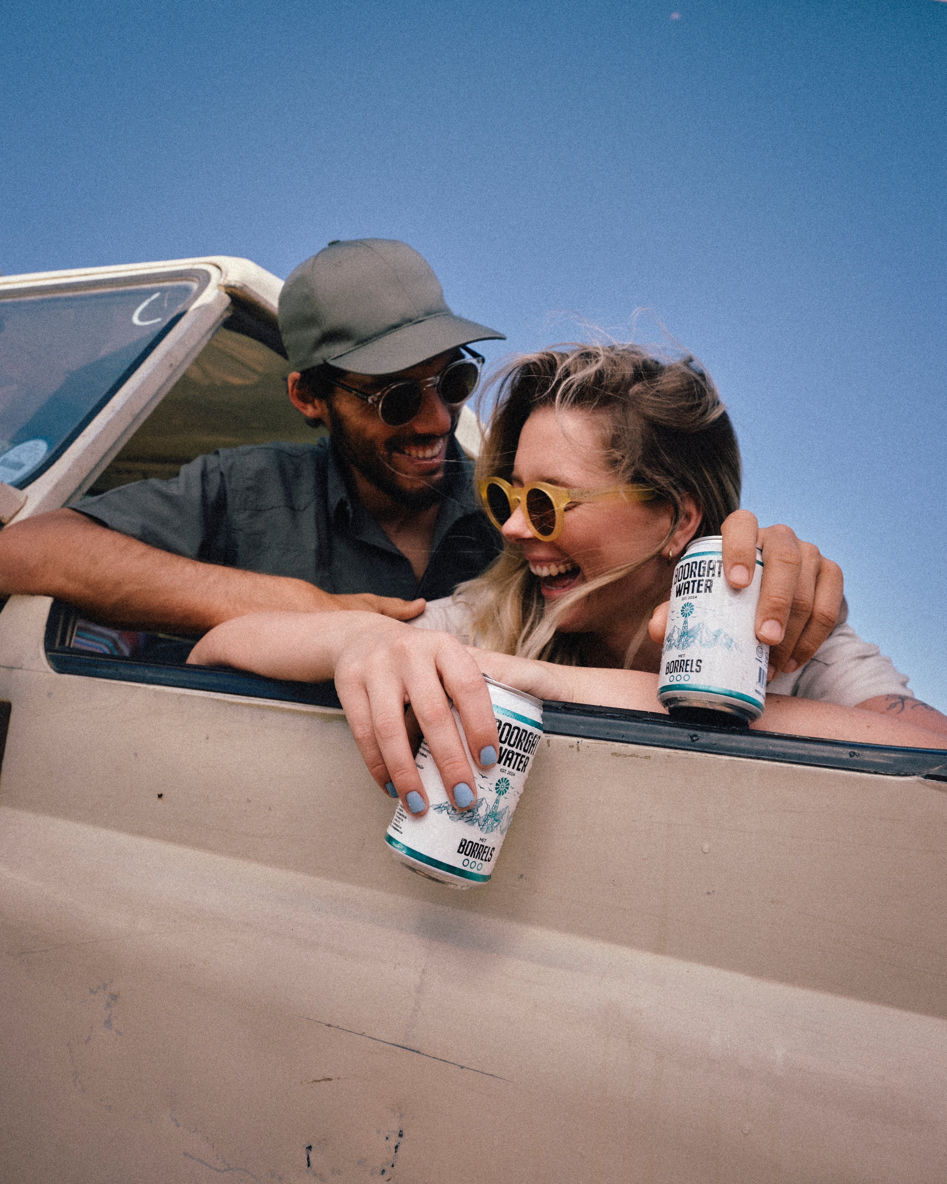 Two people in a vehicle holding water cans with a clear blue sky background