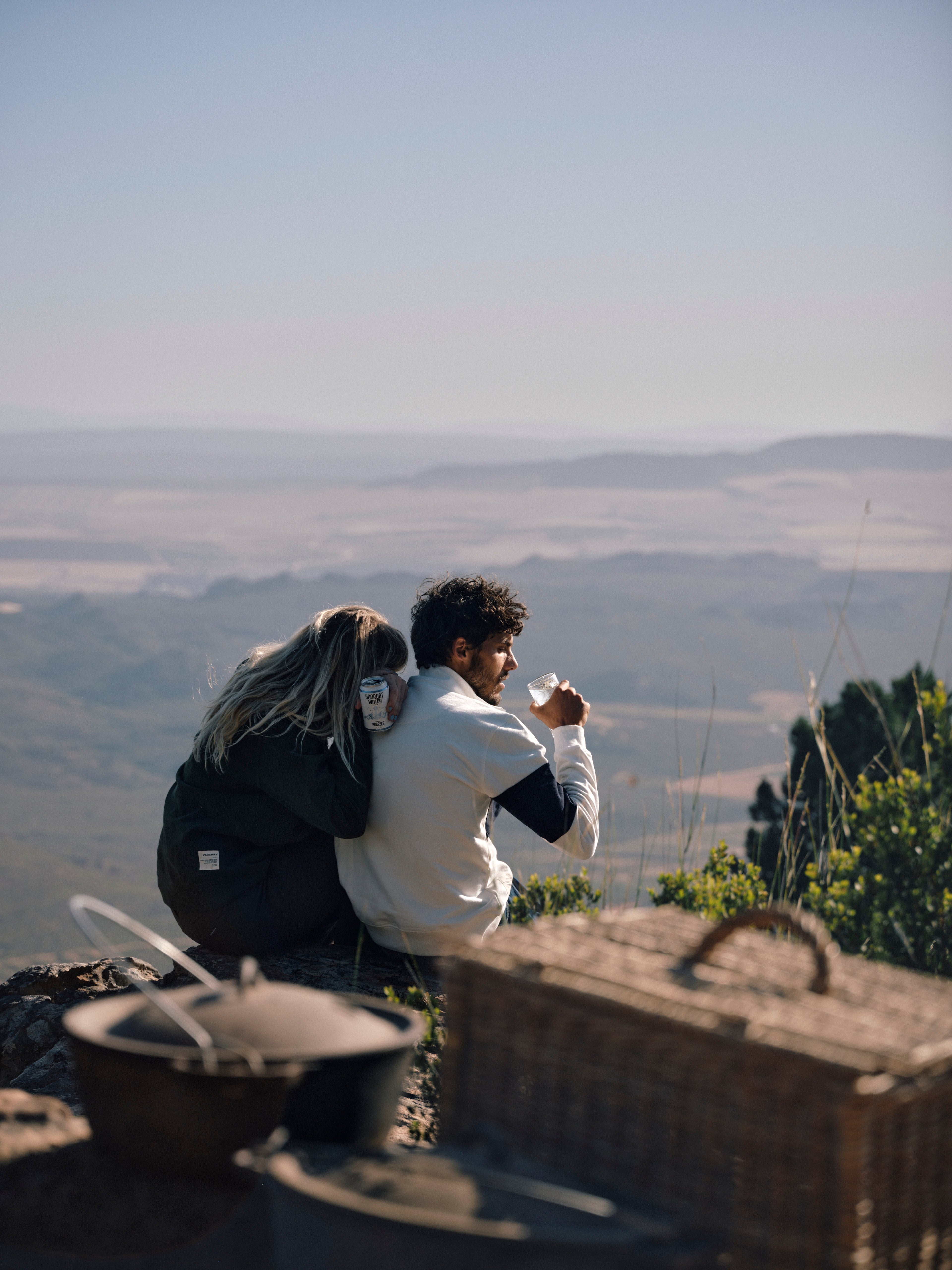 Two people sitting on a hilltop with a scenic view of fields and mountains.