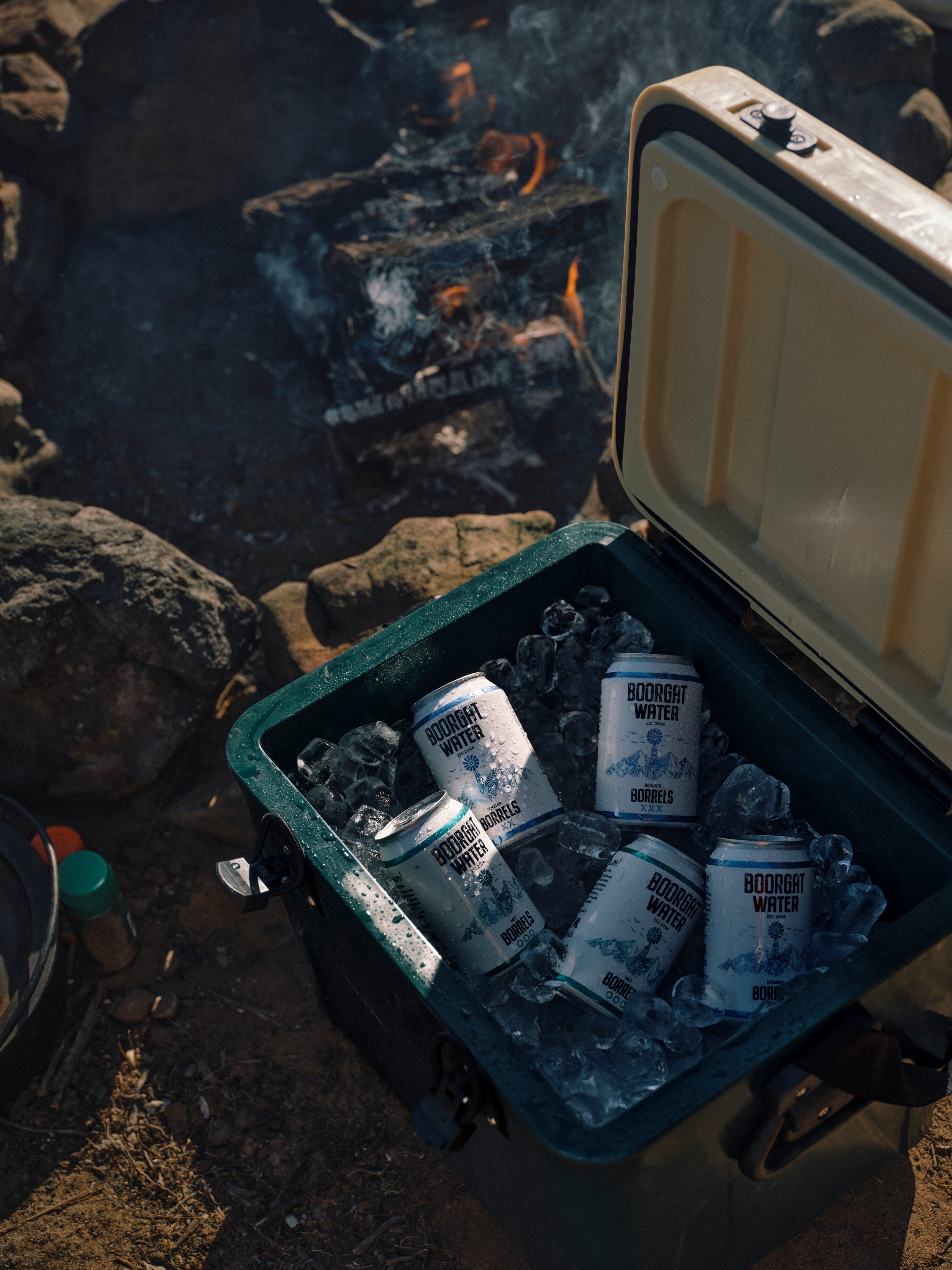 Open cooler with Boorgat Water cans and ice near a campfire